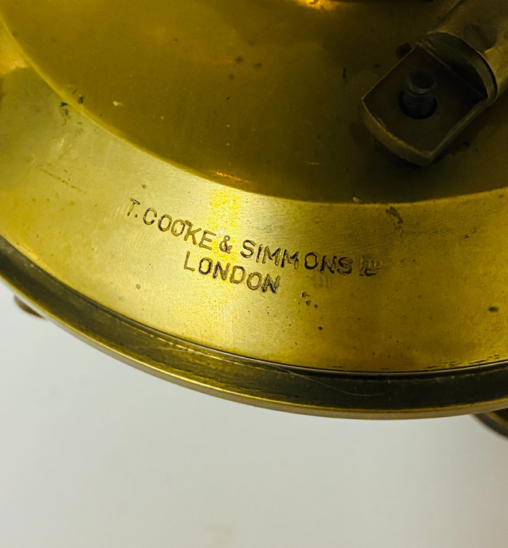 An antique brass surveyors theodolite featuring a central sighting telescope, spirit levels, and knurled adjustment screws on a circular base. View III