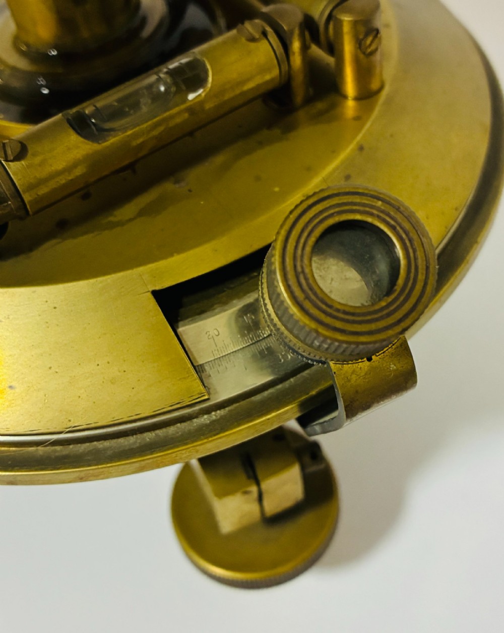 An antique brass surveyors theodolite featuring a central sighting telescope, spirit levels, and knurled adjustment screws on a circular base. View IV