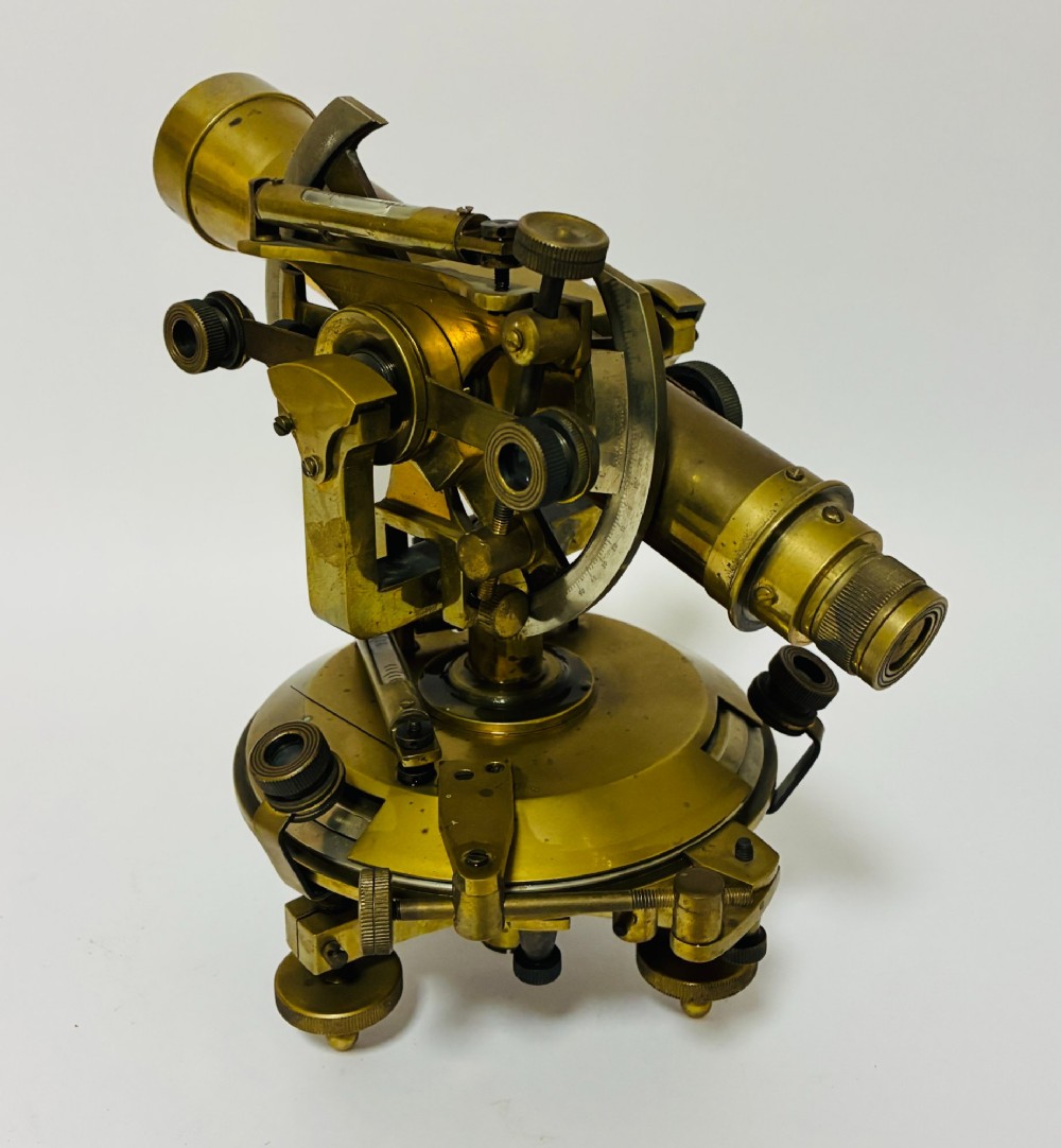 An antique brass surveyors theodolite featuring a central sighting telescope, spirit levels, and knurled adjustment screws on a circular base. View VI