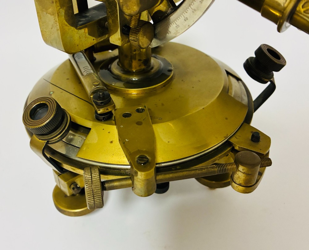 An antique brass surveyors theodolite featuring a central sighting telescope, spirit levels, and knurled adjustment screws on a circular base. View VII