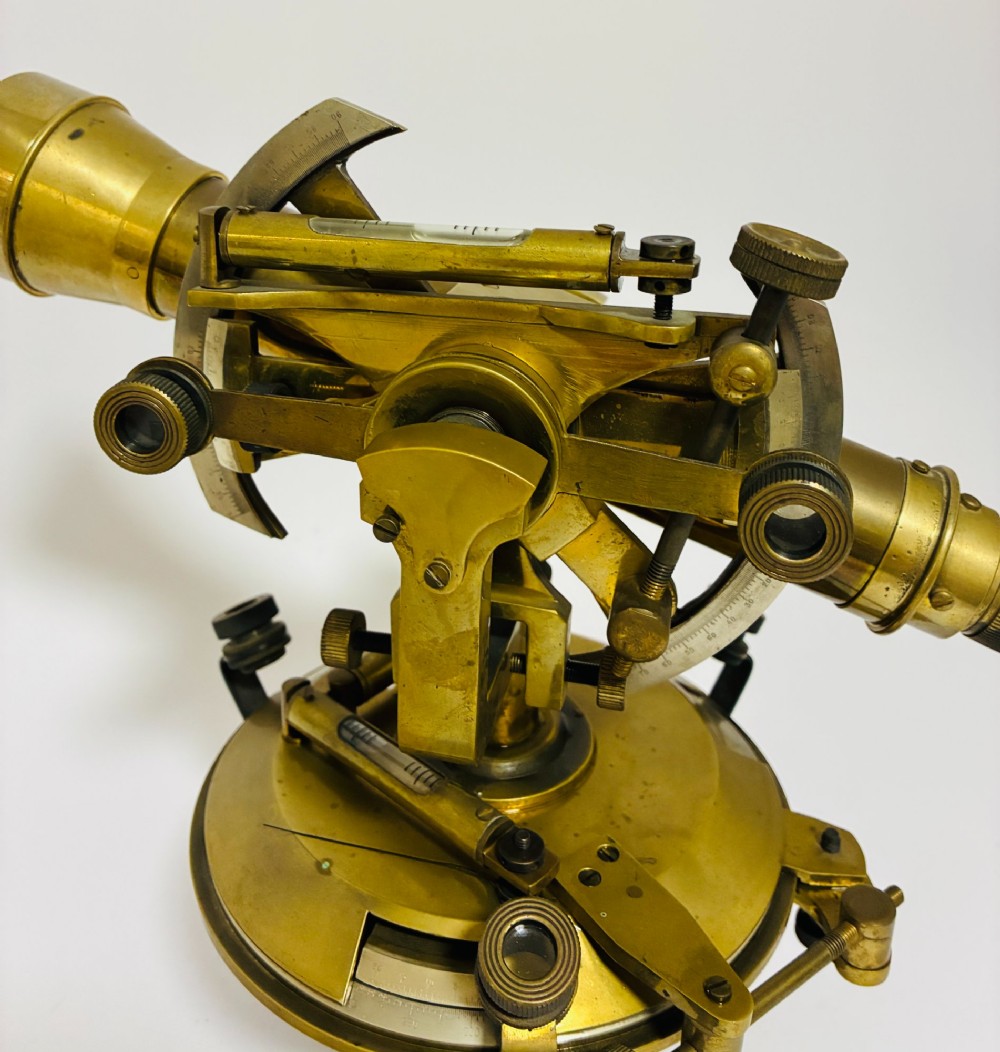 An antique brass surveyors theodolite featuring a central sighting telescope, spirit levels, and knurled adjustment screws on a circular base. View IX