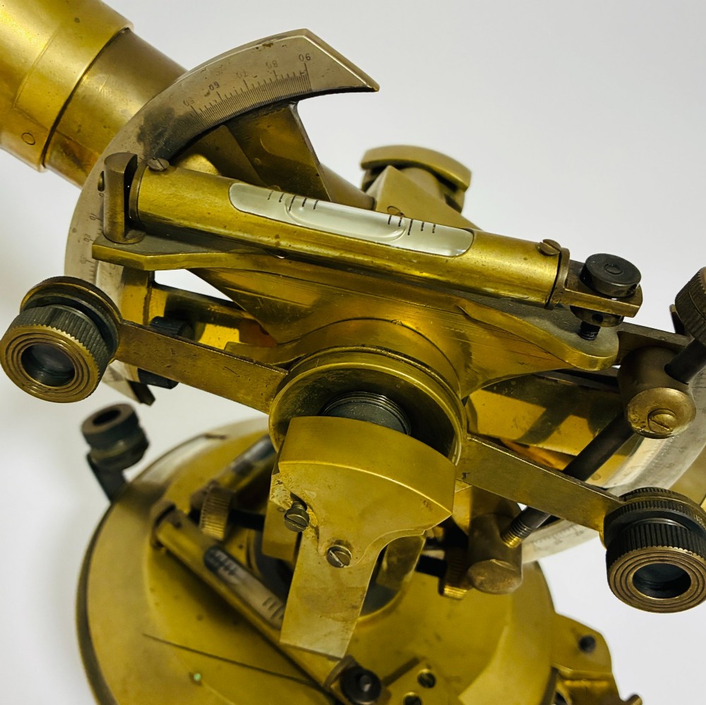 An antique brass surveyors theodolite featuring a central sighting telescope, spirit levels, and knurled adjustment screws on a circular base. View X