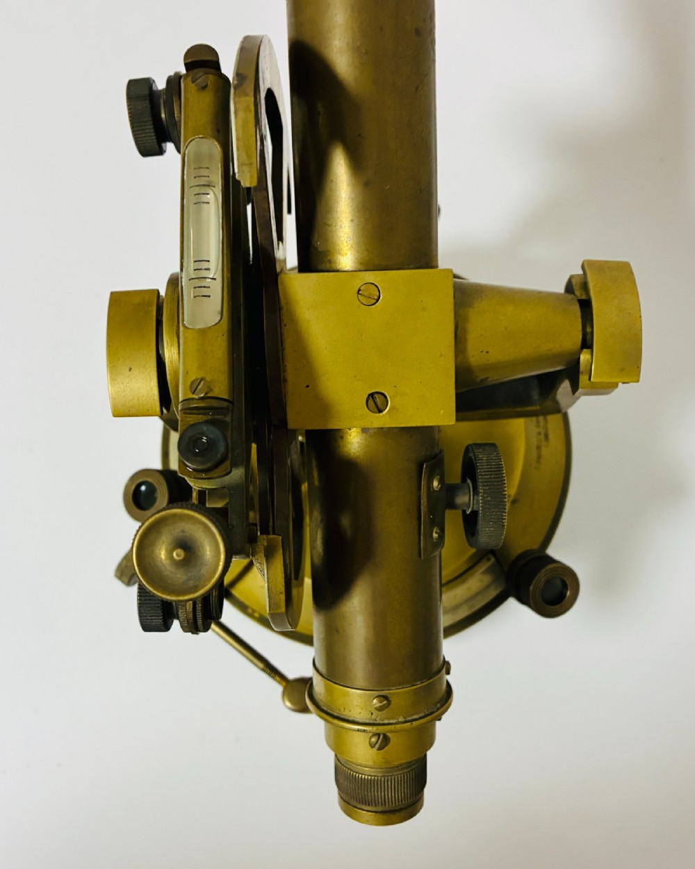 An antique brass surveyors theodolite featuring a central sighting telescope, spirit levels, and knurled adjustment screws on a circular base. View XI
