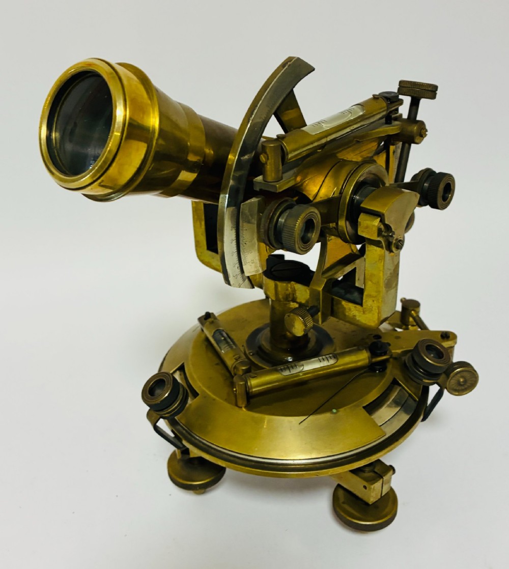 An antique brass surveyors theodolite featuring a central sighting telescope, spirit levels, and knurled adjustment screws on a circular base. View XII