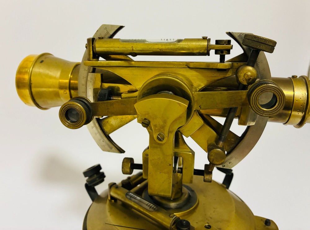 An antique brass surveyors theodolite featuring a central sighting telescope, spirit levels, and knurled adjustment screws on a circular base. View XIII