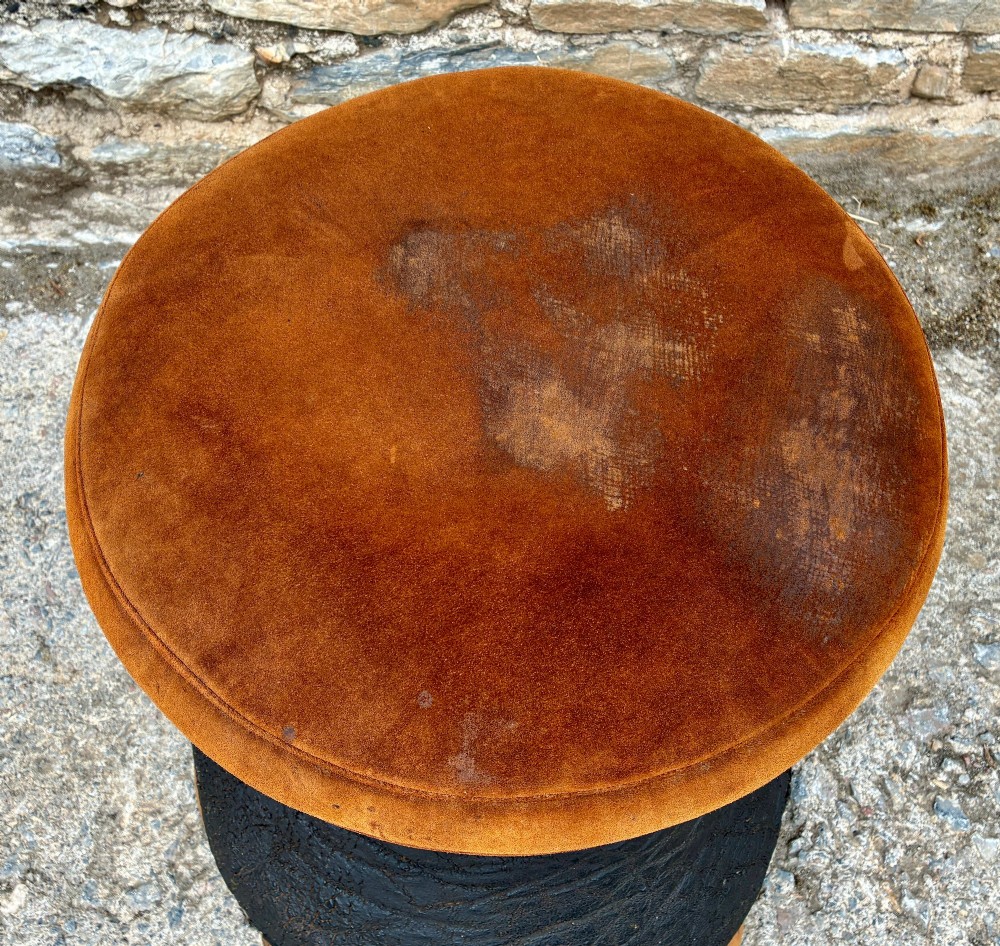An antique taxidermy elephant foot converted into a footstool, featuring dark textured hide with preserved base toenails and a cushioned tan suede seat. View II