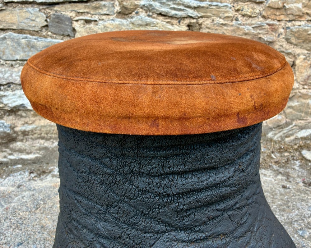 An antique taxidermy elephant foot converted into a footstool, featuring dark textured hide with preserved base toenails and a cushioned tan suede seat. View IX