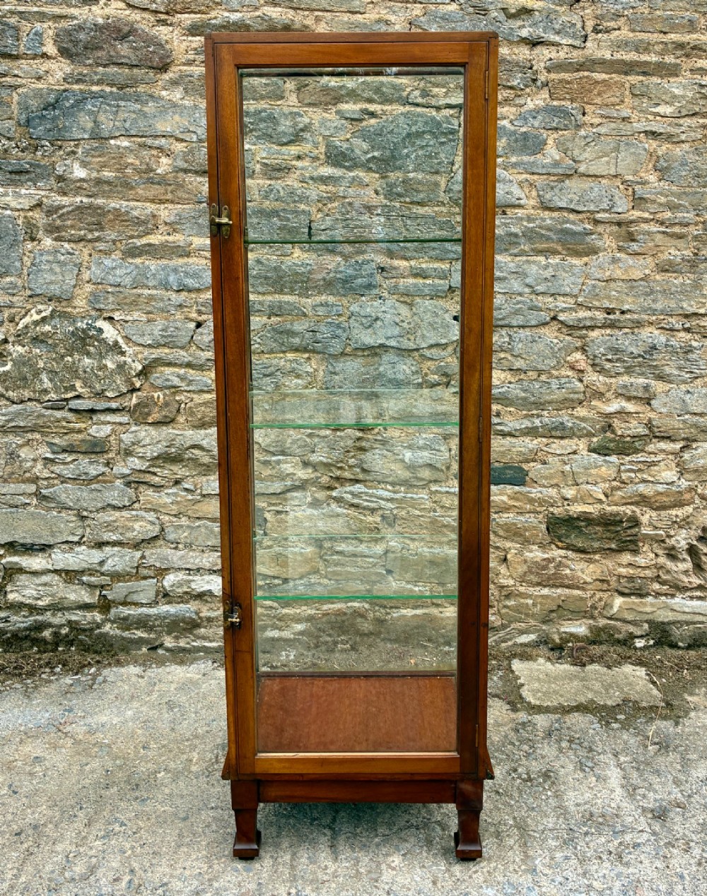 A tall, slim mahogany shop display cabinet featuring glass side panels, a single glazed door, three interior glass shelves, and brass catches.