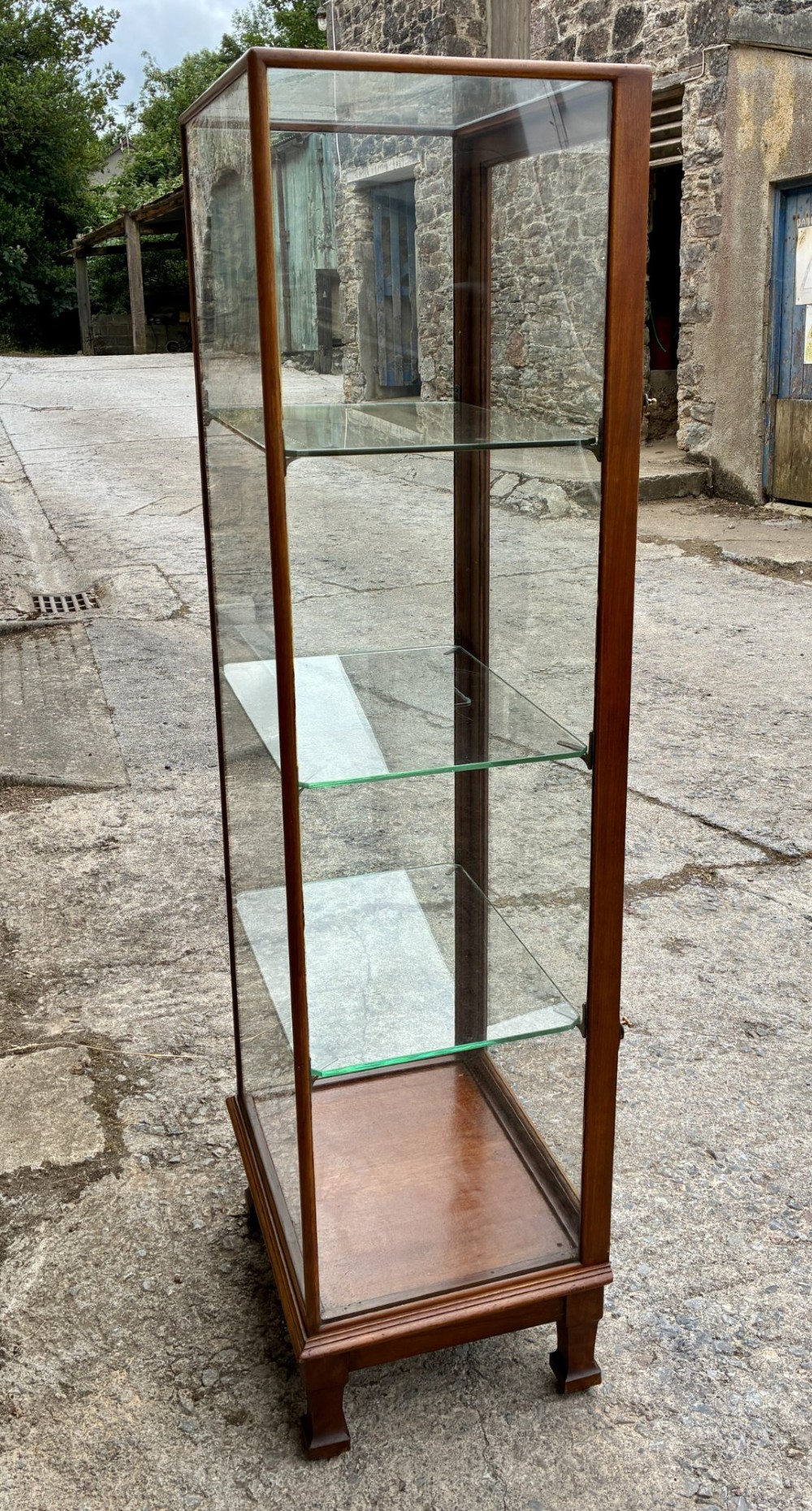 A tall, slim mahogany shop display cabinet featuring glass side panels, a single glazed door, three interior glass shelves, and brass catches. View IV