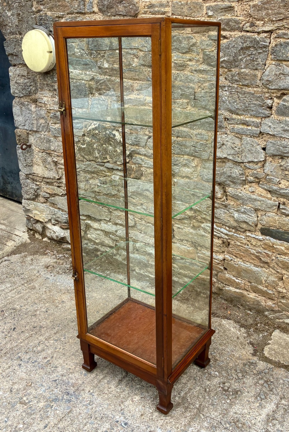 A tall, slim mahogany shop display cabinet featuring glass side panels, a single glazed door, three interior glass shelves, and brass catches. View V