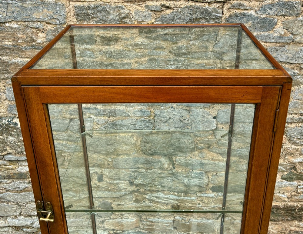 A tall, slim mahogany shop display cabinet featuring glass side panels, a single glazed door, three interior glass shelves, and brass catches. View VI