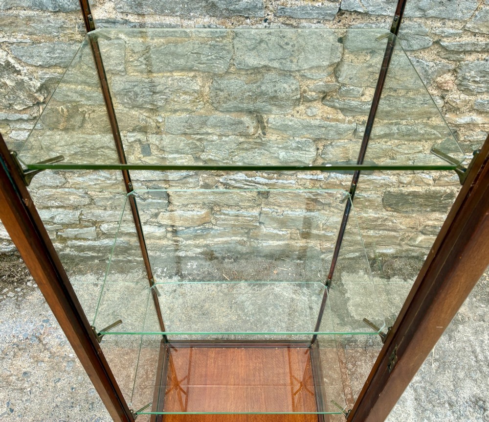 A tall, slim mahogany shop display cabinet featuring glass side panels, a single glazed door, three interior glass shelves, and brass catches. View XIII