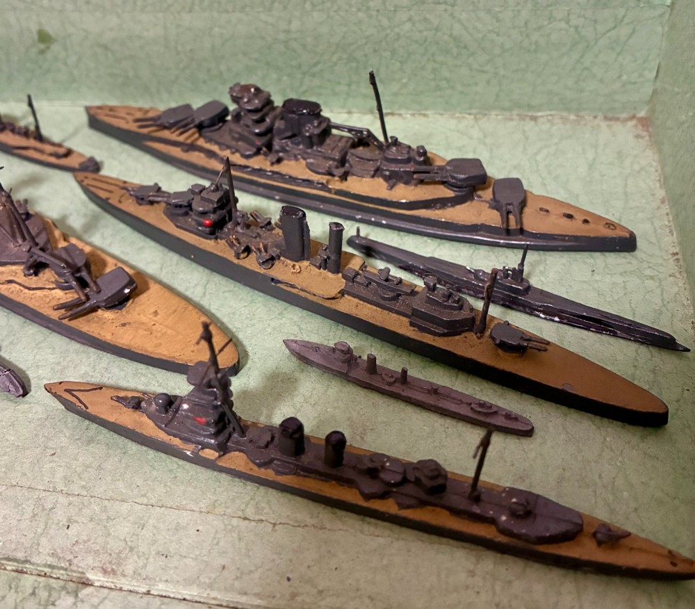 A vintage green cardboard box containing a set of miniature diecast metal model warships of the British Navy. View IV