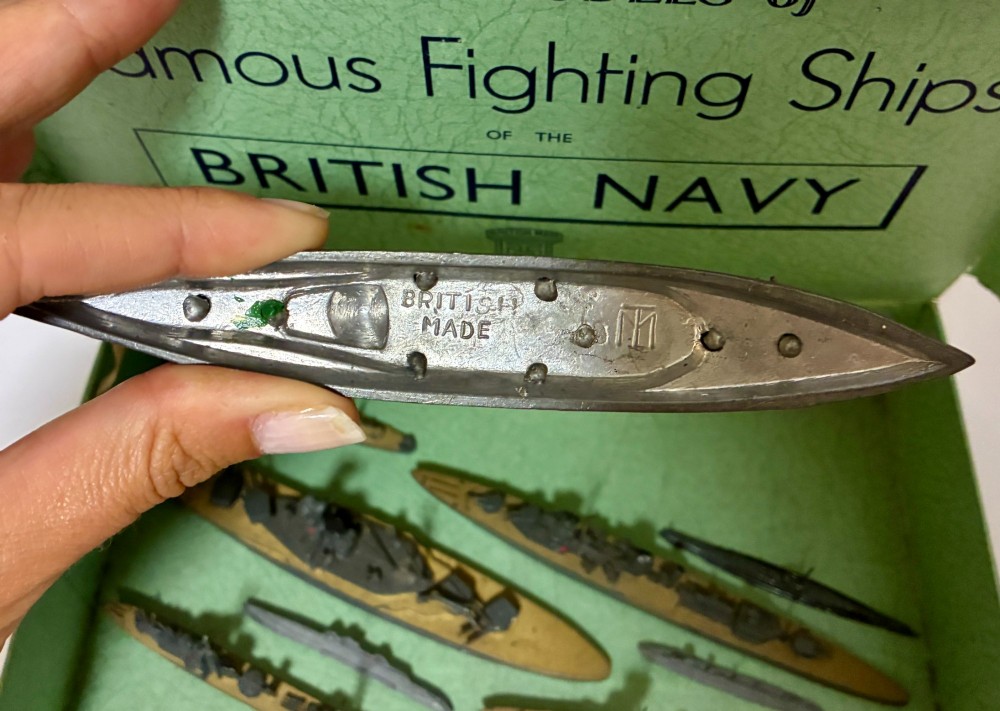 A vintage green cardboard box containing a set of miniature diecast metal model warships of the British Navy. View X