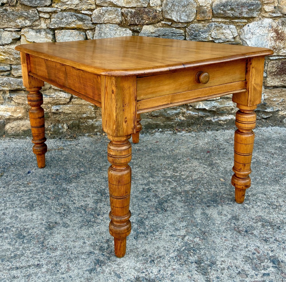 An antique pine farmhouse table featuring turned legs, a frieze drawer with a wooden knob, and a warm timber finish.