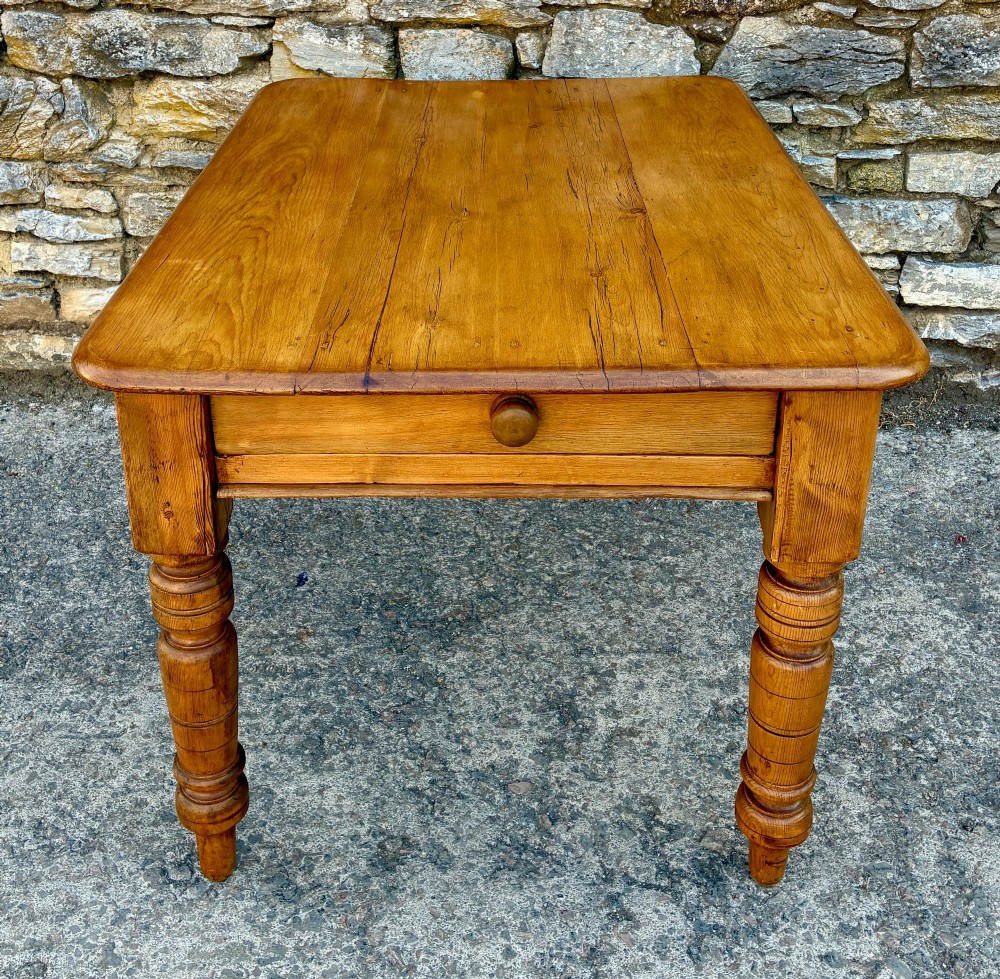 An antique pine farmhouse table featuring turned legs, a frieze drawer with a wooden knob, and a warm timber finish. View II