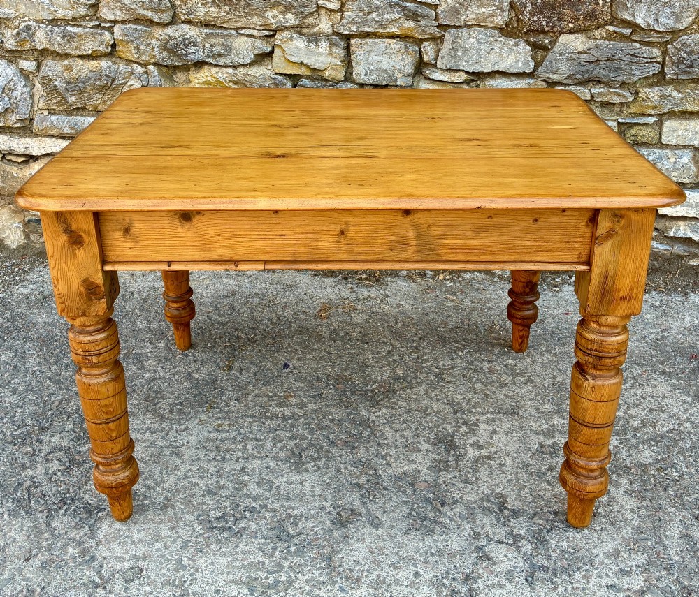 An antique pine farmhouse table featuring turned legs, a frieze drawer with a wooden knob, and a warm timber finish. View V