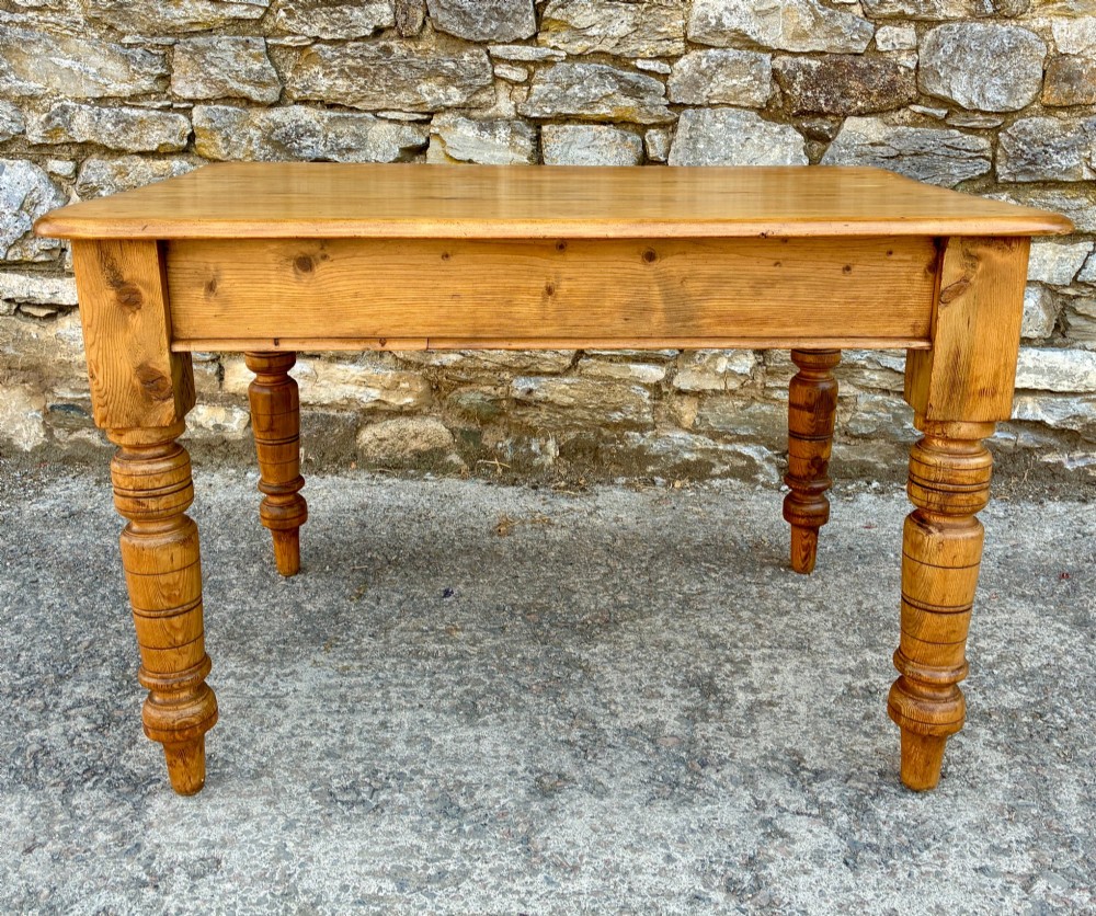An antique pine farmhouse table featuring turned legs, a frieze drawer with a wooden knob, and a warm timber finish. View VI