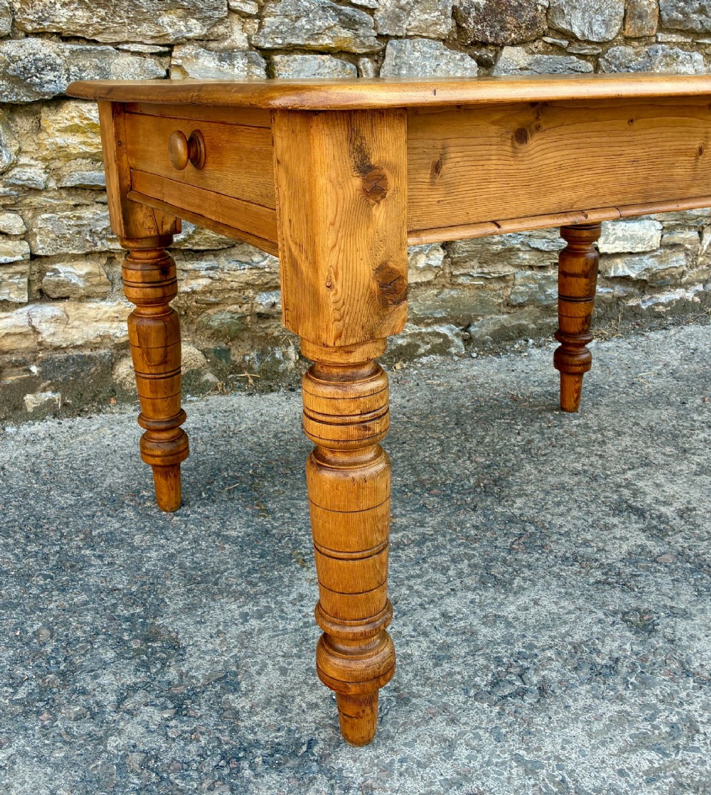 An antique pine farmhouse table featuring turned legs, a frieze drawer with a wooden knob, and a warm timber finish. View VII