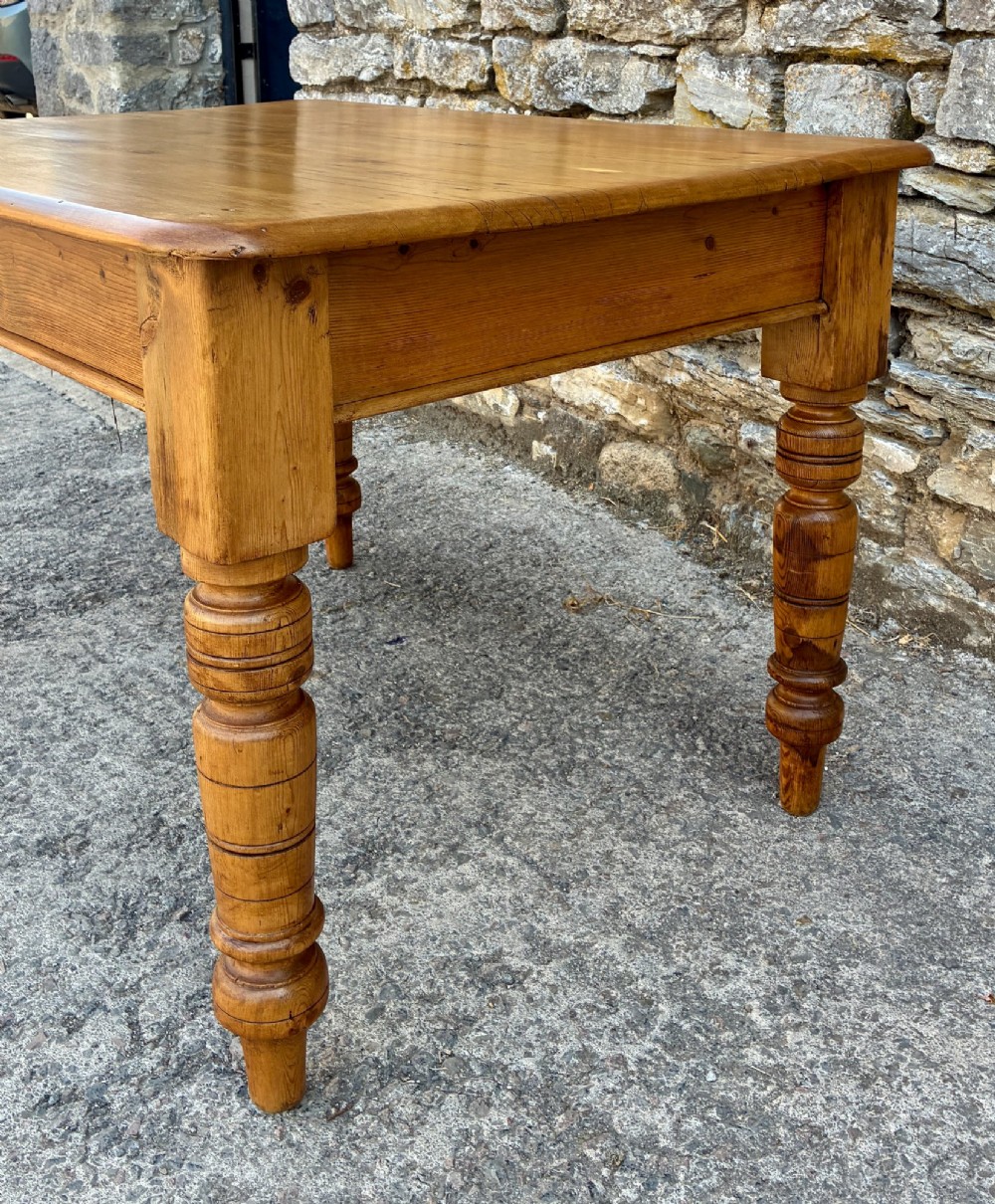 An antique pine farmhouse table featuring turned legs, a frieze drawer with a wooden knob, and a warm timber finish. View VIII