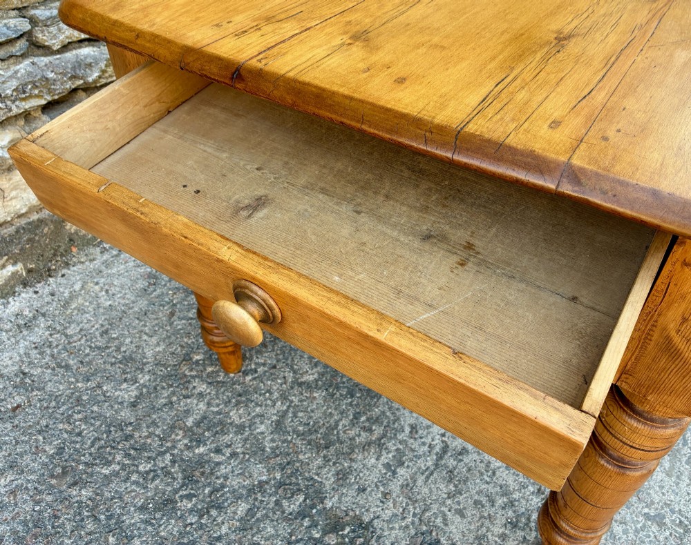 An antique pine farmhouse table featuring turned legs, a frieze drawer with a wooden knob, and a warm timber finish. View X