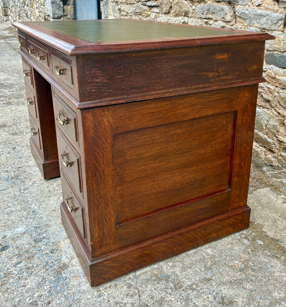 An Edwardian oak pedestal desk featuring a green leather writing surface, nine drawers with brass handles, and twin pedestals on plinth bases. View VIII