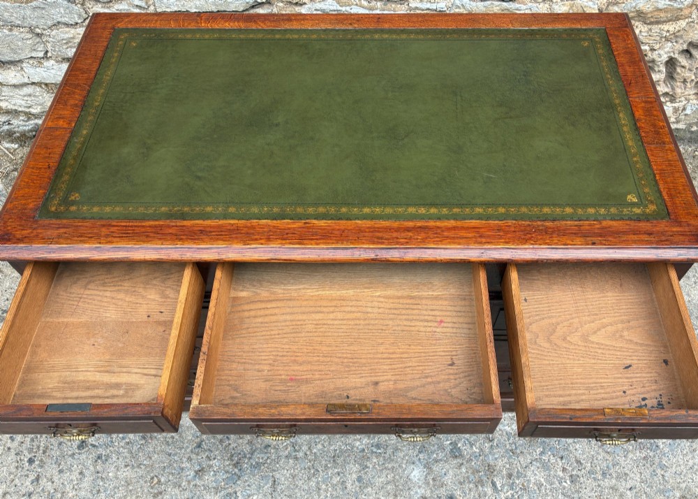 An Edwardian oak pedestal desk featuring a green leather writing surface, nine drawers with brass handles, and twin pedestals on plinth bases. View IX