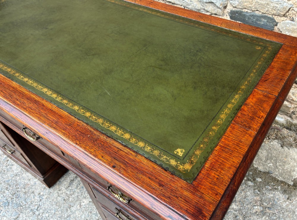 An Edwardian oak pedestal desk featuring a green leather writing surface, nine drawers with brass handles, and twin pedestals on plinth bases. View XIV