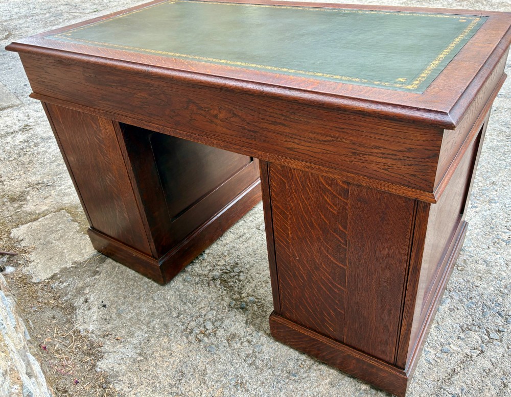 An Edwardian oak pedestal desk featuring a green leather writing surface, nine drawers with brass handles, and twin pedestals on plinth bases. View XV