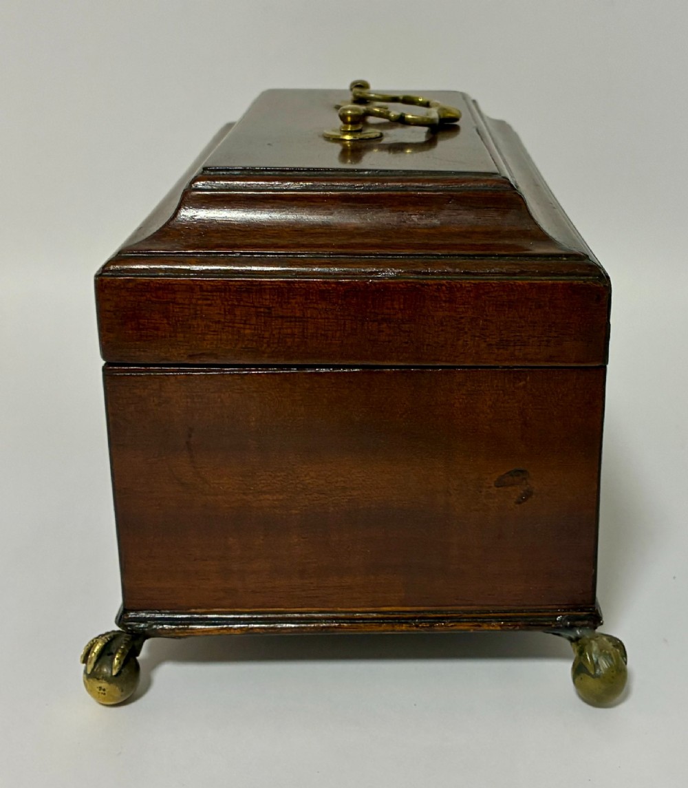 A rectangular George III mahogany tea caddy with a stepped lid, top brass swing handle, pierced brass escutcheon with key, and four brass claw-and-ball feet. View IX