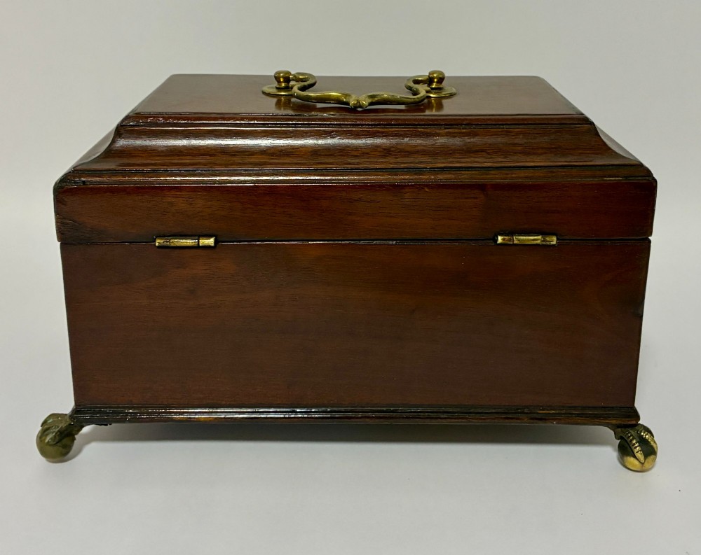 A rectangular George III mahogany tea caddy with a stepped lid, top brass swing handle, pierced brass escutcheon with key, and four brass claw-and-ball feet. View X