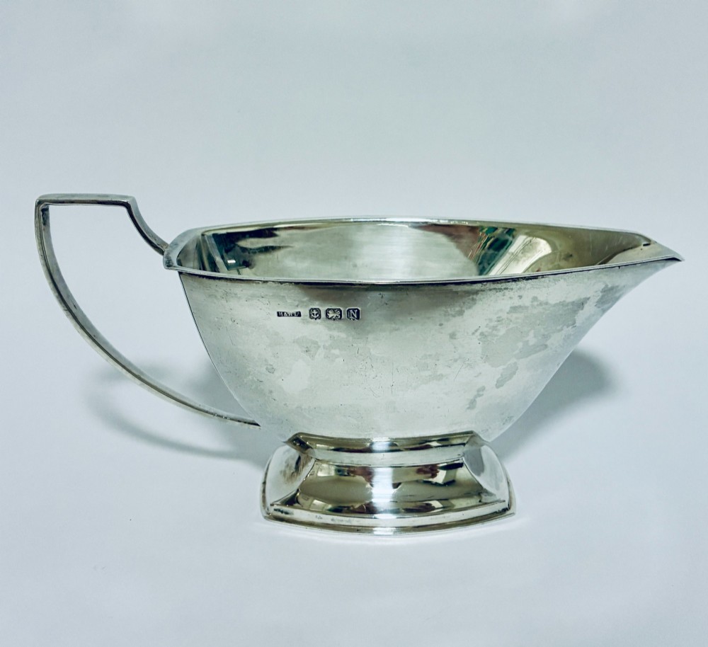 An Art Deco sterling silver sauce boat featuring an angular handle, stepped pedestal base, and clear English hallmarks on the side.