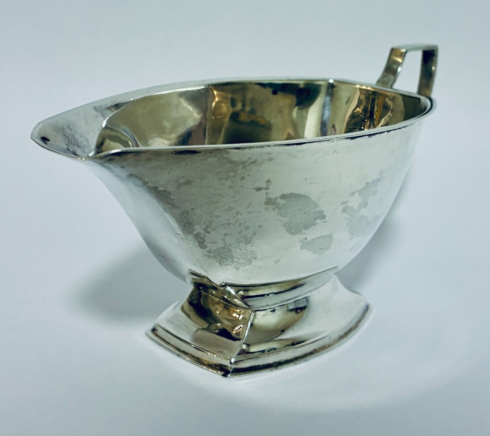 An Art Deco sterling silver sauce boat featuring an angular handle, stepped pedestal base, and clear English hallmarks on the side. View III