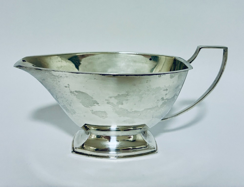 An Art Deco sterling silver sauce boat featuring an angular handle, stepped pedestal base, and clear English hallmarks on the side. View IV