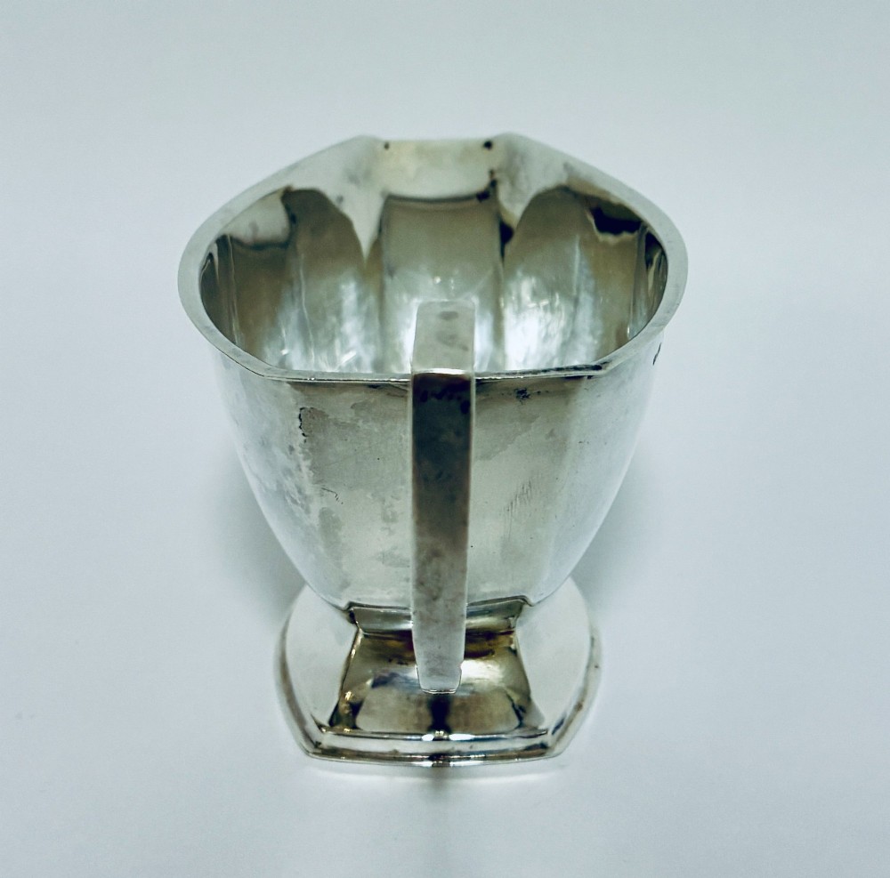 An Art Deco sterling silver sauce boat featuring an angular handle, stepped pedestal base, and clear English hallmarks on the side. View V