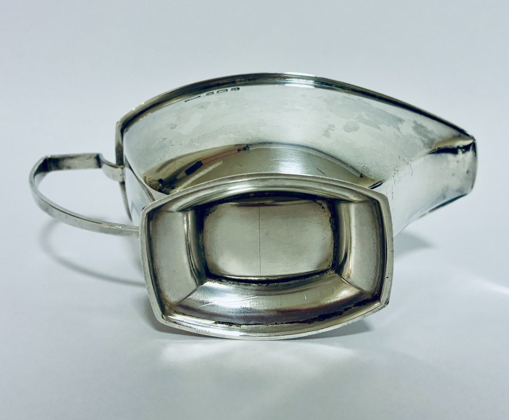 An Art Deco sterling silver sauce boat featuring an angular handle, stepped pedestal base, and clear English hallmarks on the side. View VII