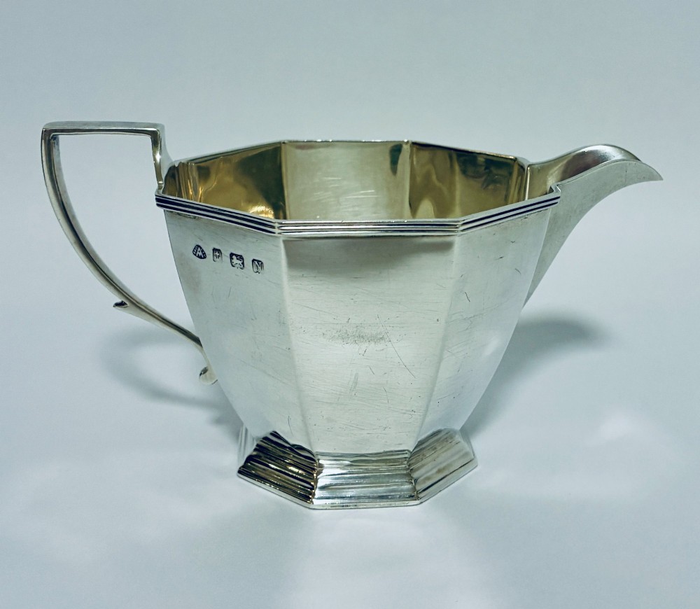 An octagonal sterling silver milk jug featuring an angular handle, a pronounced pouring spout, and visible stamped hallmarks on the front facet.