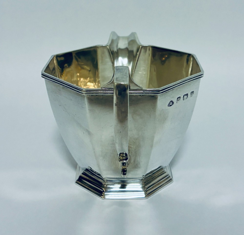 An octagonal sterling silver milk jug featuring an angular handle, a pronounced pouring spout, and visible stamped hallmarks on the front facet. View III
