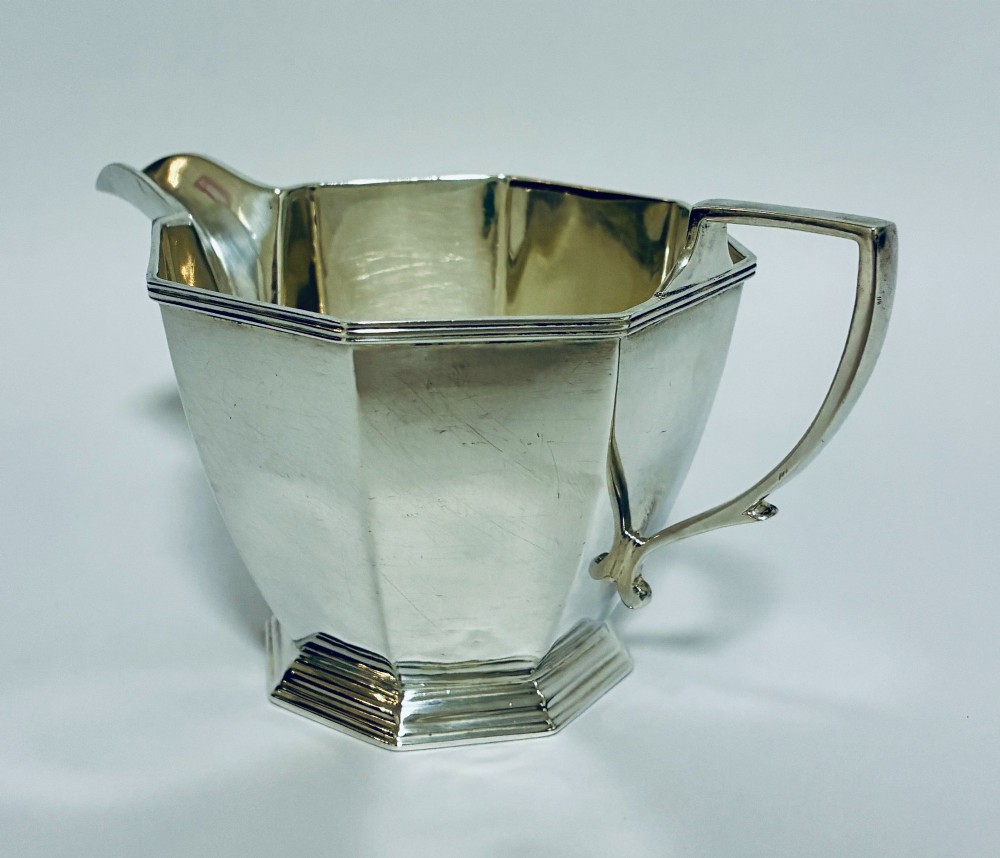 An octagonal sterling silver milk jug featuring an angular handle, a pronounced pouring spout, and visible stamped hallmarks on the front facet. View IV