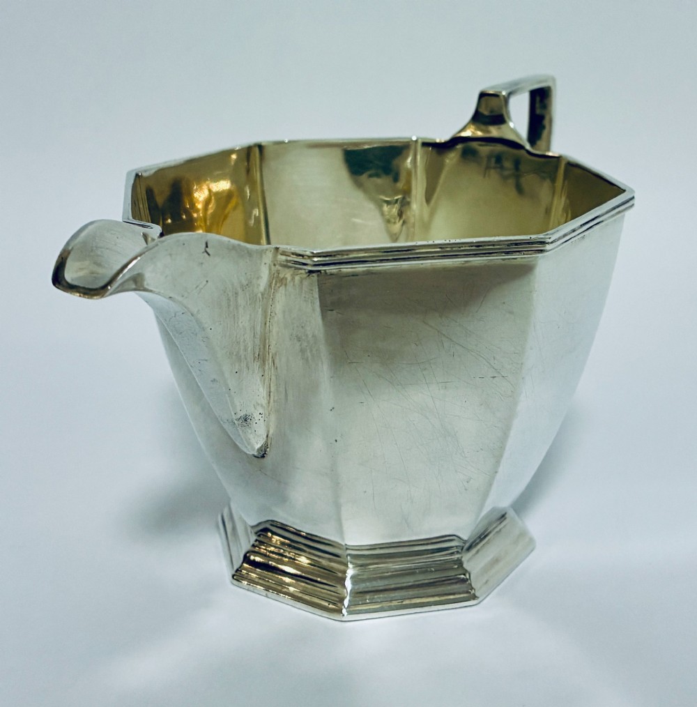 An octagonal sterling silver milk jug featuring an angular handle, a pronounced pouring spout, and visible stamped hallmarks on the front facet. View VI