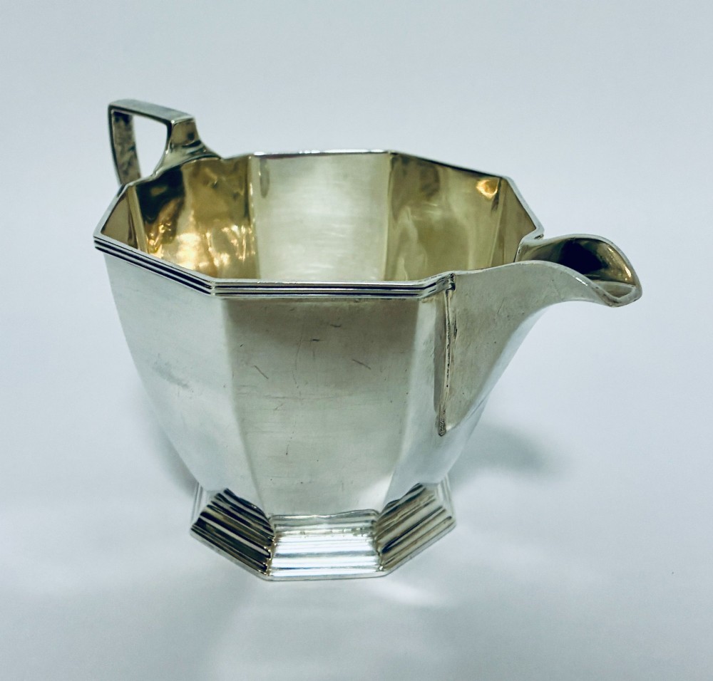 An octagonal sterling silver milk jug featuring an angular handle, a pronounced pouring spout, and visible stamped hallmarks on the front facet. View VIII