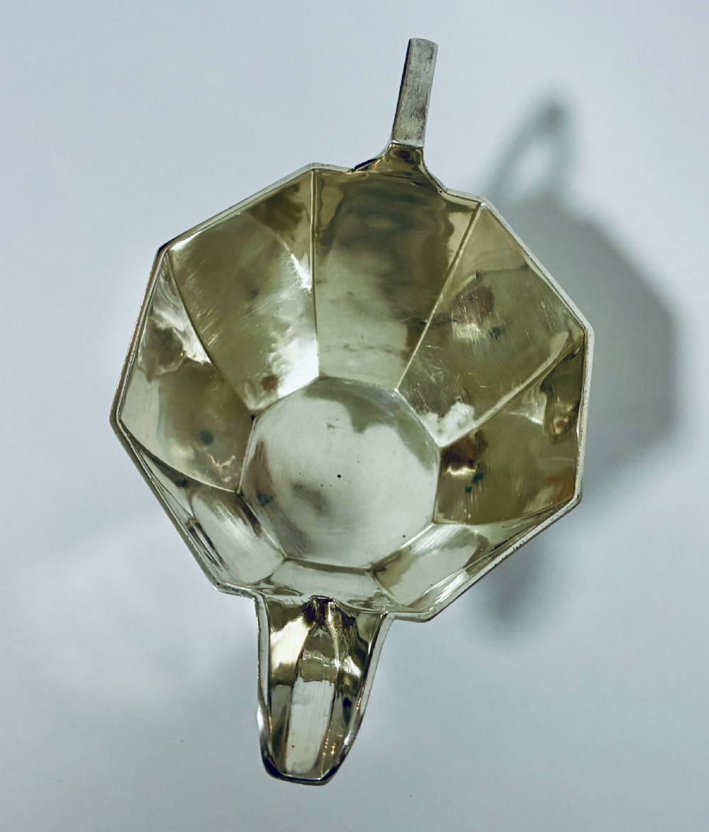 An octagonal sterling silver milk jug featuring an angular handle, a pronounced pouring spout, and visible stamped hallmarks on the front facet. View IX