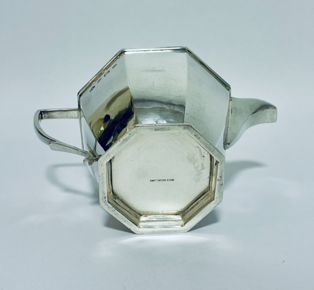 An octagonal sterling silver milk jug featuring an angular handle, a pronounced pouring spout, and visible stamped hallmarks on the front facet. View X