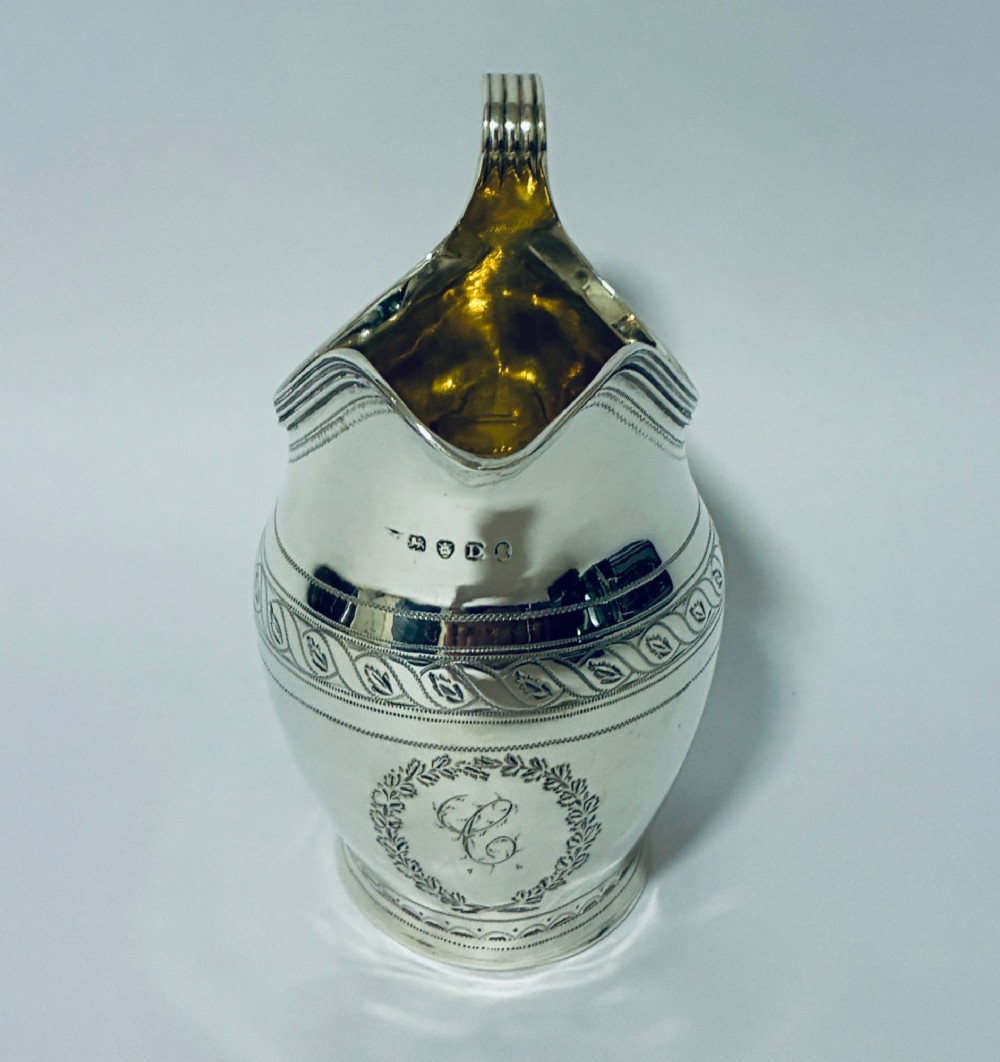 A Georgian sterling silver cream jug featuring a high reeded loop handle, engraved foliate bands around the body, and a gilded interior finish. View III