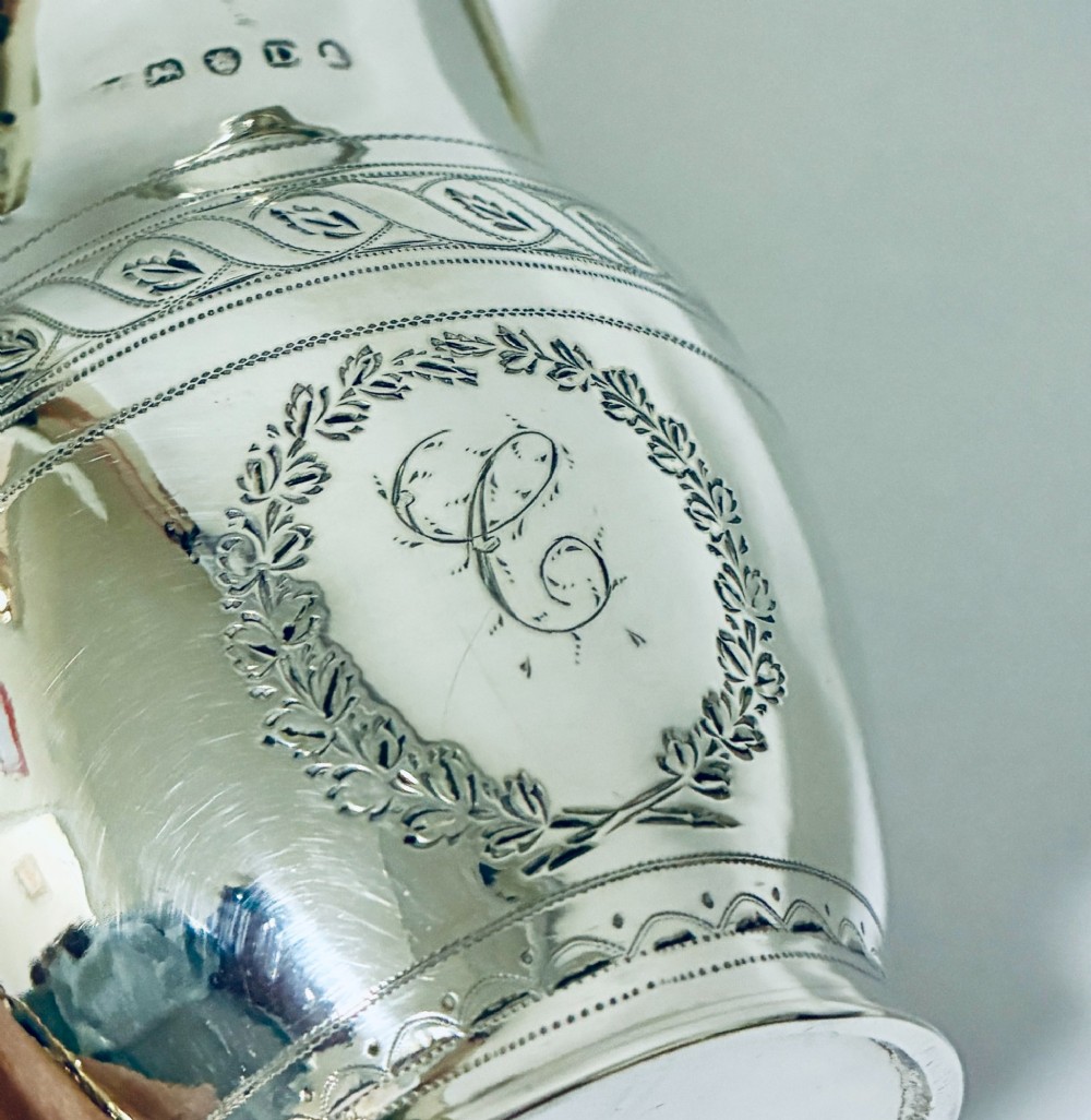 A Georgian sterling silver cream jug featuring a high reeded loop handle, engraved foliate bands around the body, and a gilded interior finish. View VIII