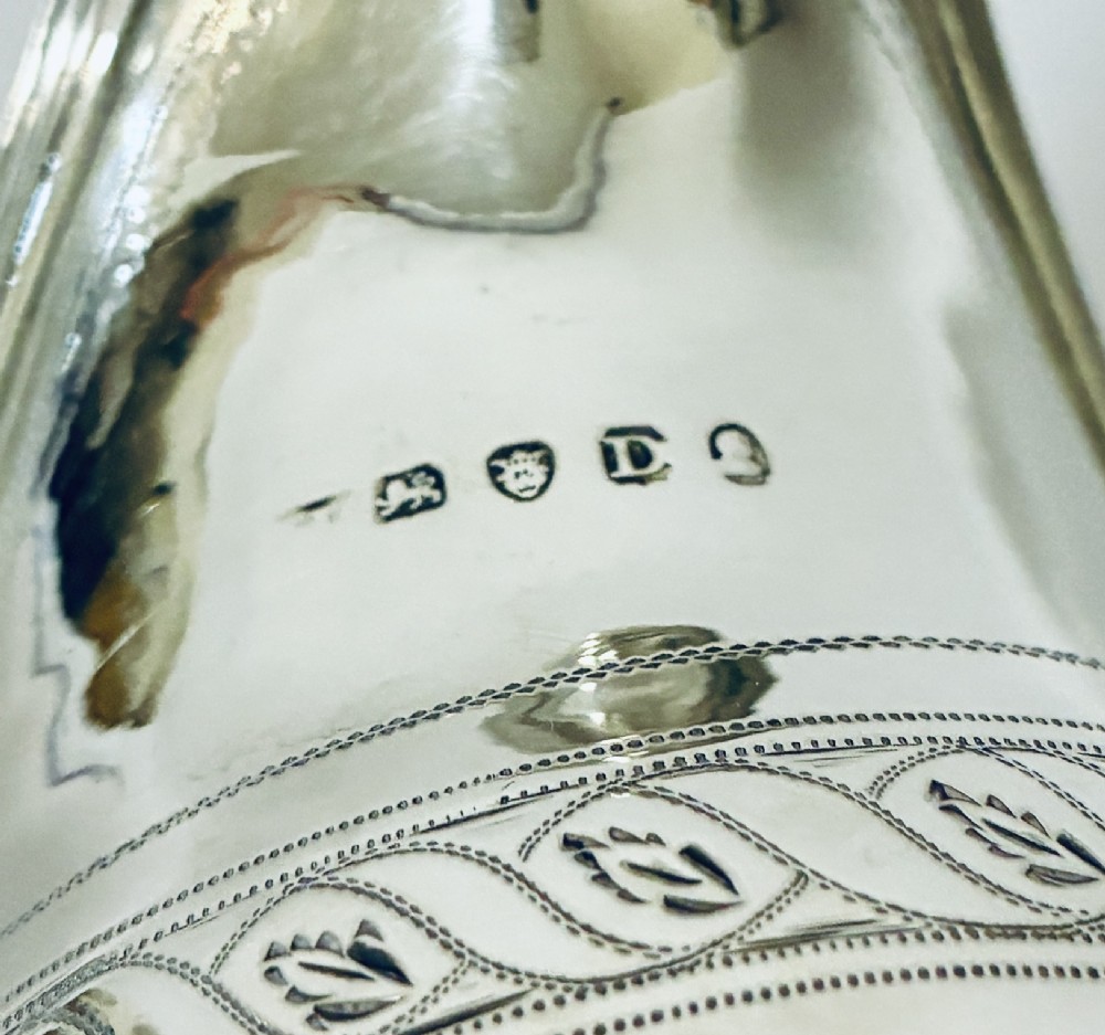 A Georgian sterling silver cream jug featuring a high reeded loop handle, engraved foliate bands around the body, and a gilded interior finish. View IX