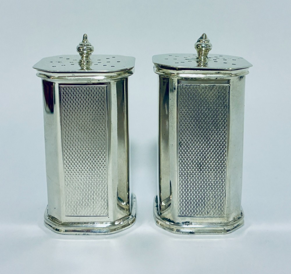 A pair of matching silver pepper pots with canted corners, engine-turned central panels, and perforated tops with decorative finials. View II