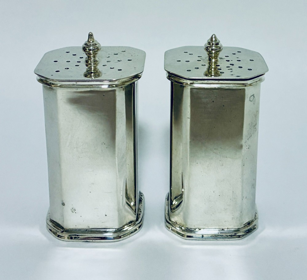 A pair of matching silver pepper pots with canted corners, engine-turned central panels, and perforated tops with decorative finials. View III