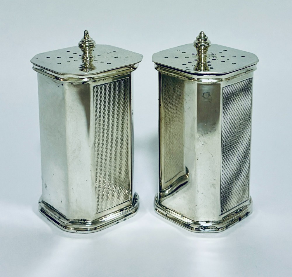 A pair of matching silver pepper pots with canted corners, engine-turned central panels, and perforated tops with decorative finials. View IV