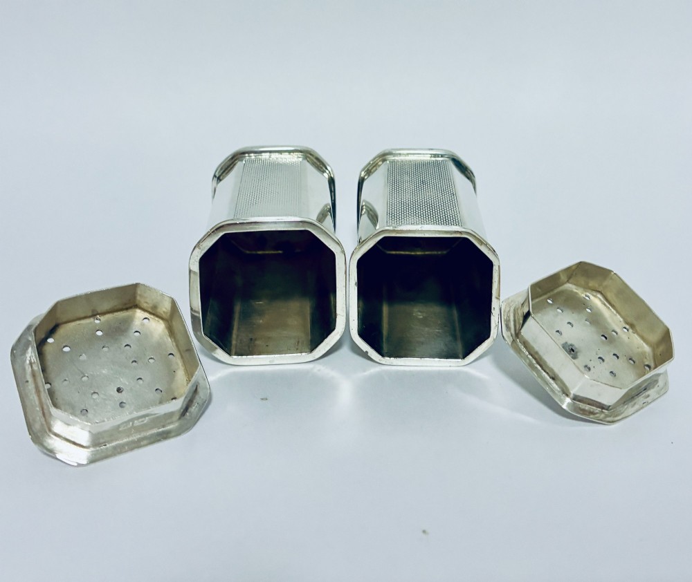 A pair of matching silver pepper pots with canted corners, engine-turned central panels, and perforated tops with decorative finials. View VII